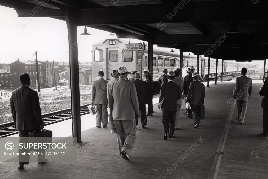 1960s MEN IN SUITS AND HATS BUSINESSMEN BACK VIEW OF SUBURBAN STATION PASSENGERS WAITING FOR REGIONAL COMMUTER TRAIN