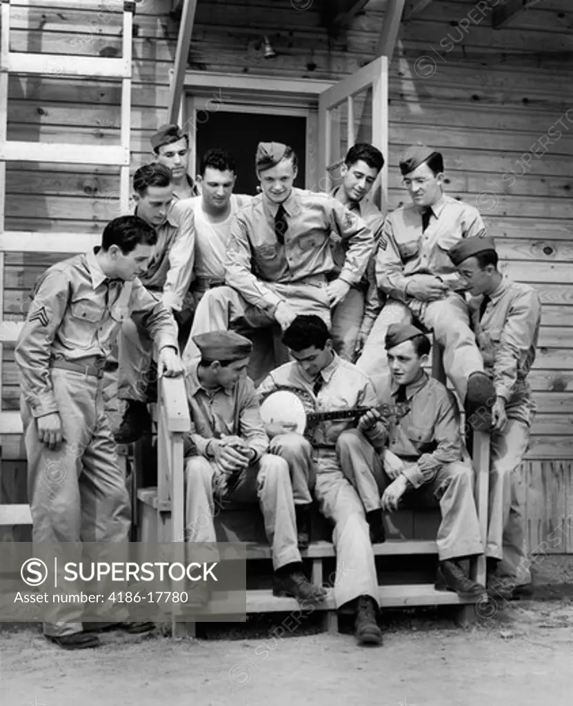 1940s GROUP OF SOLDIER SITTING ON STEPS OF BARRACKS LISTENING TO MAN PLAYING BANJO