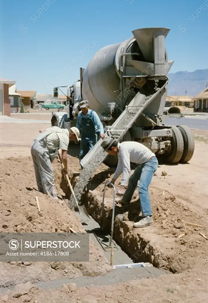 1960s 3 WORKERS POURING CONCRETE FOR FOUNDATION OF HOUSE IN ALBUQUERQUE NEW MEXICO