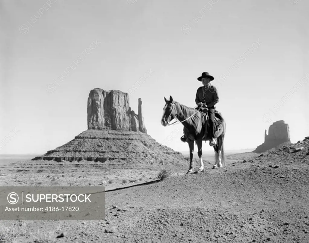 NAVAJO INDIAN IN COWBOY HAT ON HORSEBACK WITH MONUMENT VALLEY ROCK FORMATIONS IN BACKGROUND
