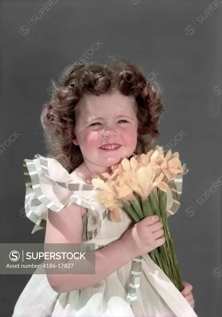 1940s 1950s PORTRAIT SMILING BRUNETTE GIRL HOLDING BOUQUET OF YELLOW JONQUILS LOOKING AT CAMERA