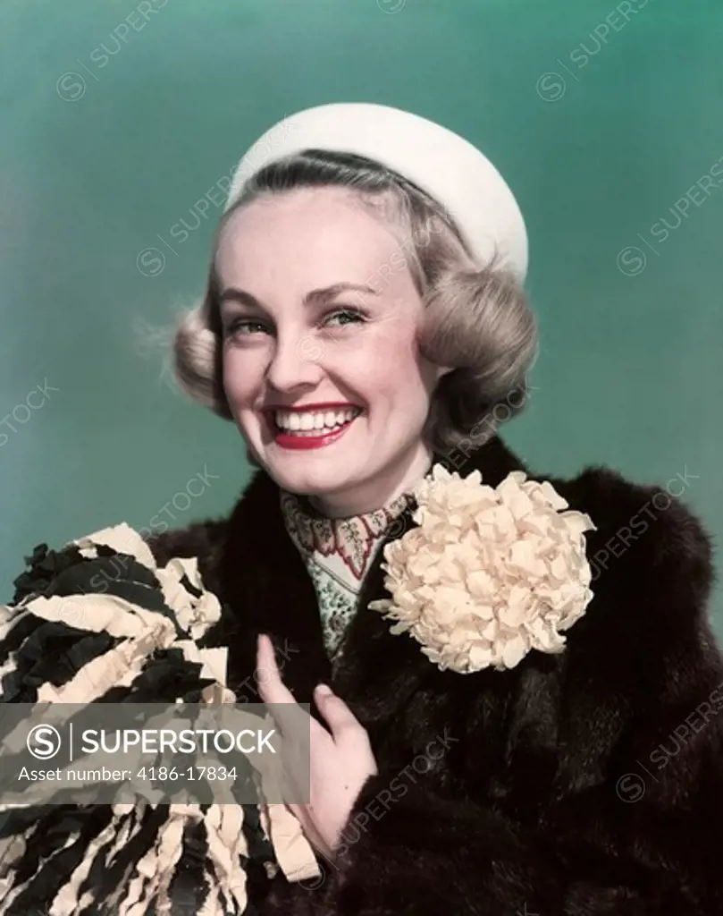 1940s 1950s PORTRAIT SMILING BLOND WOMAN WEARING FUR COAT WITH MUM FLOWER DECORATION HOLDING POMPOM