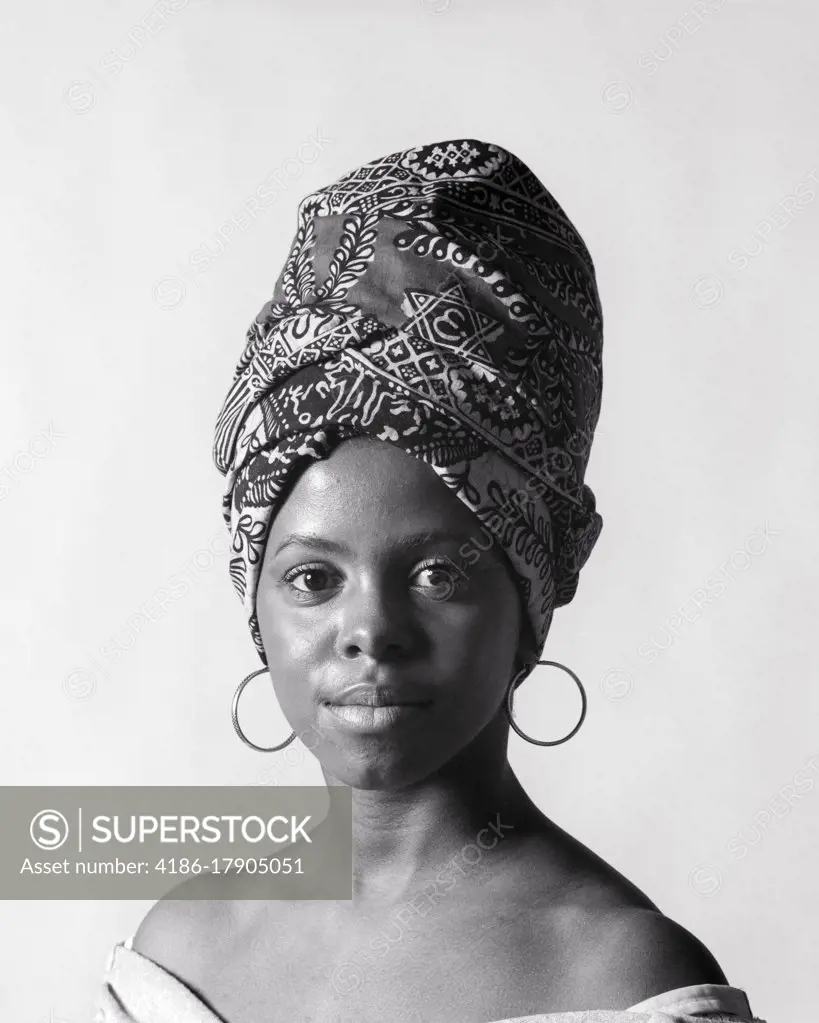 1970s PORTRAIT AFRICAN AMERICAN YOUNG WOMAN LOOKING AT CAMERA WEARING A TIGON A PRINT FABRIC HEAD-WRAP AND HOOP EARRINGS