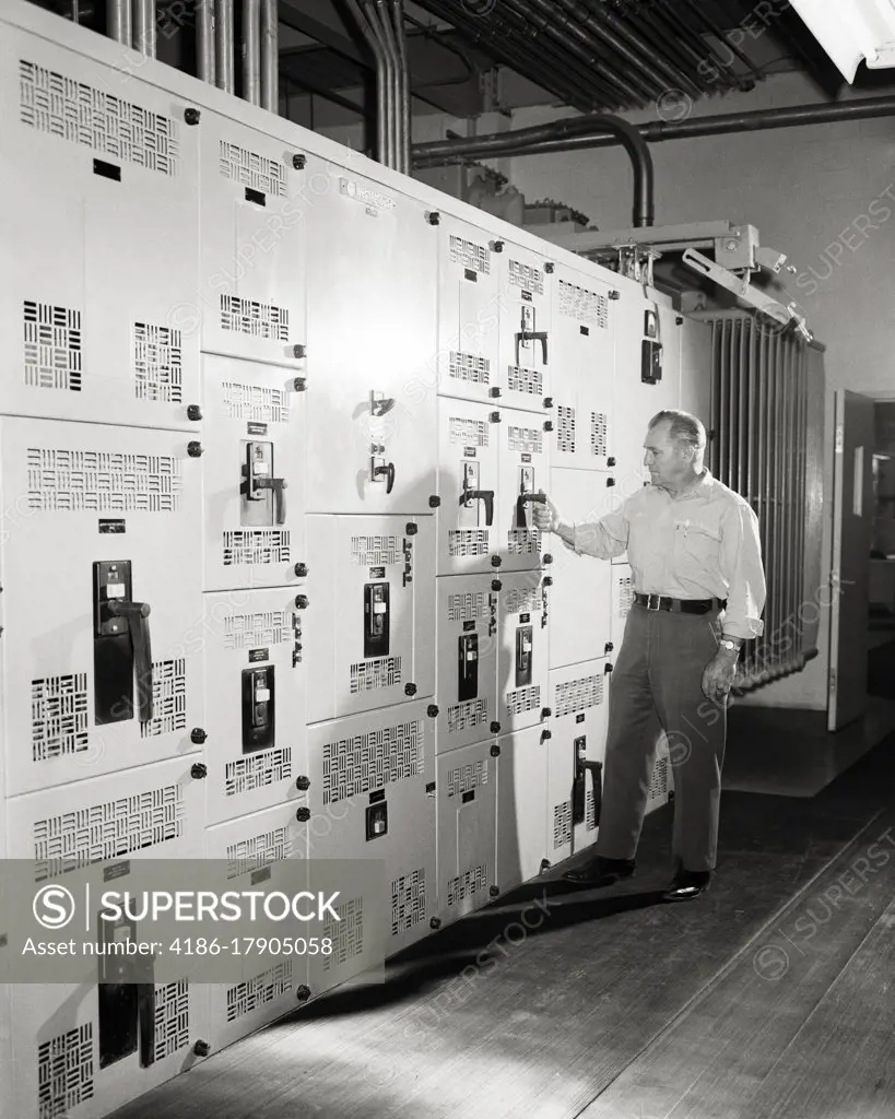 1960s MAN SUPERVISOR ENGINEER AT THE CONTROL PANELS OF MASSIVE AIR CONDITIONING SYSTEM FOR LARGE BUILDING