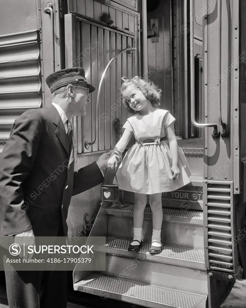 1950s MAN PASSENGER RAILROAD CONDUCTOR IN UNIFORM GREETING SMILING LITTLE GIRL WEARING DRESS AND MARY JANE SHORES ON TRAIN STEPS