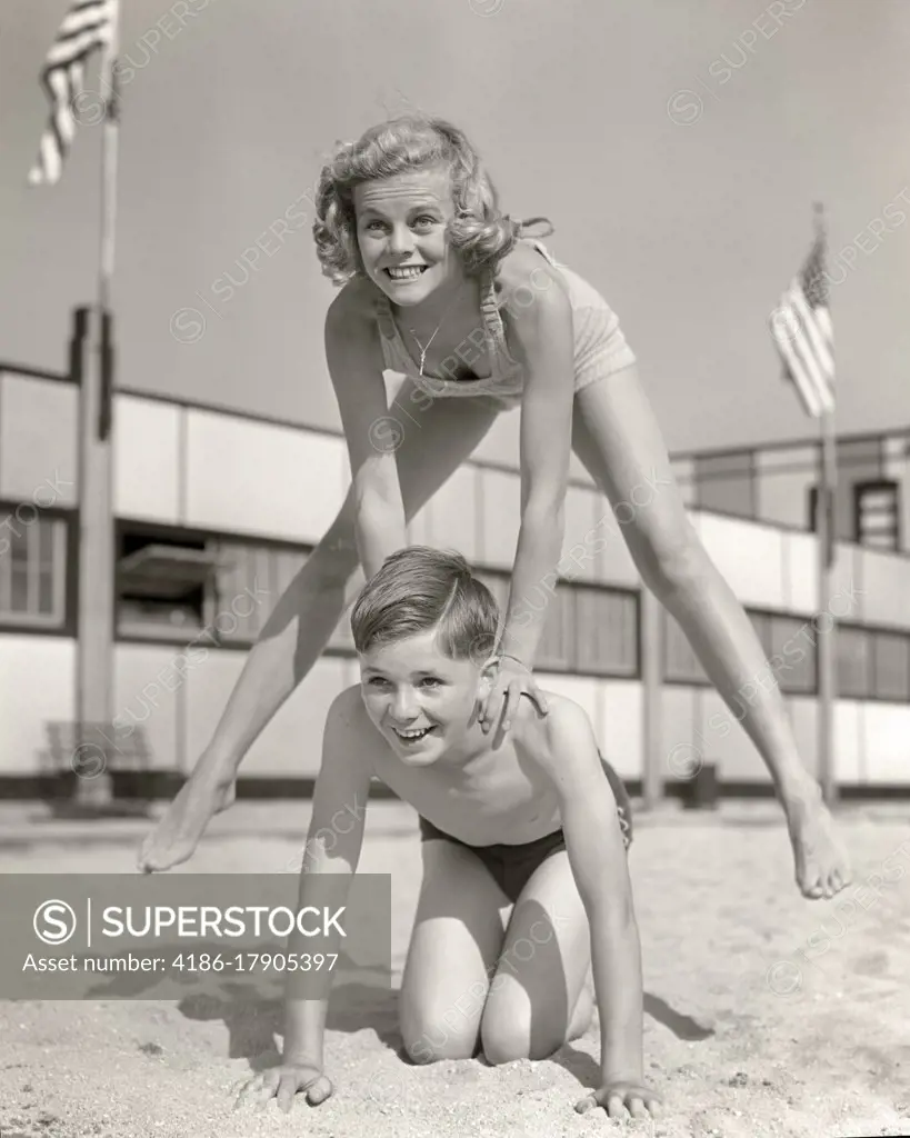 1930s 1940s SMILING GIRL AND BOY PLAYING LEAP FROG ON SAND BEACH BROTHER KNEELING BLONDE SISTER JUMPING OVER HIS BACK