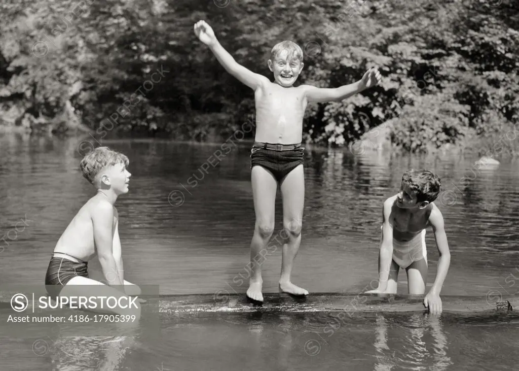 1930s 1940s THREE BOYS FRIENDS BROTHERS PLAYING TOGETHER BALANCING ON FLOATING LOG IN RURAL SWIMMING HOLE WEARING BATHING SUITS