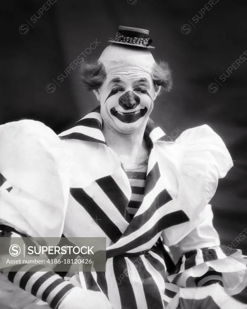 1930s SMILING BIG TOP CIRCUS WHITEFACE CLOWN LOOKING AT CAMERA WEARING TINY HAT STRIPED OVERSIZE COSTUME