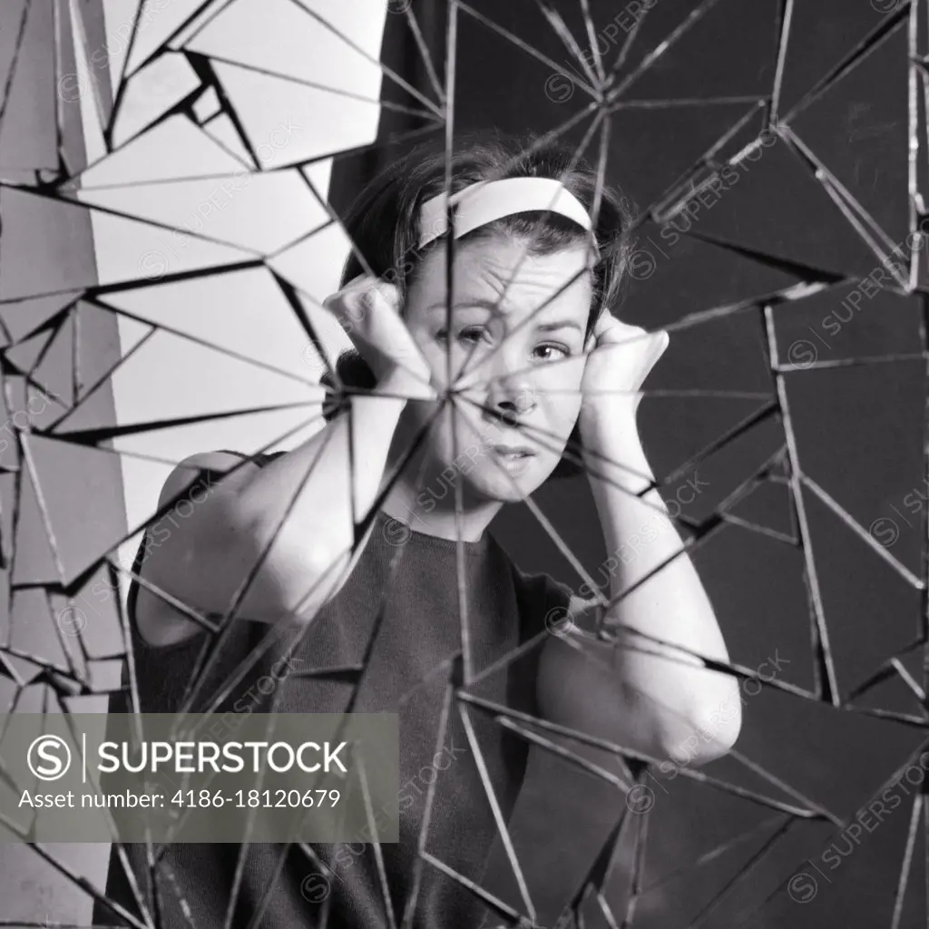 1960s 1970s DISTURBED WOMAN LOOKING AT CAMERA HOLDING HEAD IN PAIN SEEING HER REFLECTION IN SHARDS OF BROKEN MIRROR GLASS