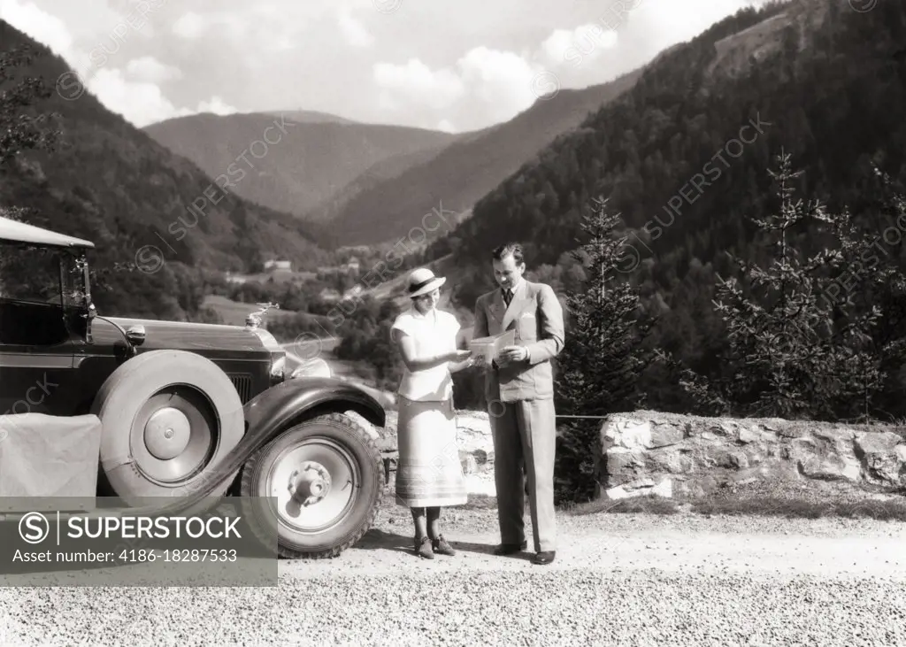 1920s 1930s MAN AND WOMAN PERHAPS LOST READING ROAD MAP STANDING BESIDE AUTOMOBILE NEAR FELDBERG IN BLACK FOREST OF GERMANY 