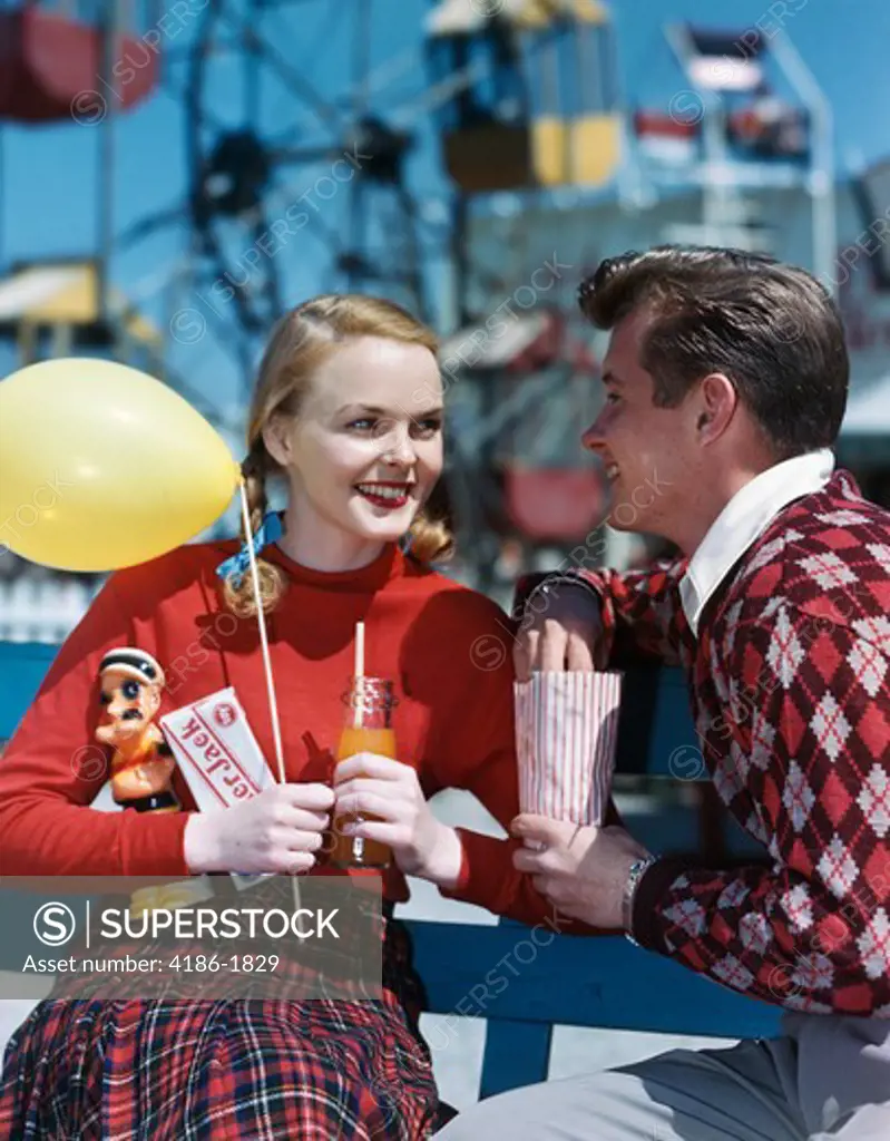 1940S 1950S Young Couple At Amusement Park Man Eating Popcorn Woman Holding Balloon And Drink And Crackerjack Box