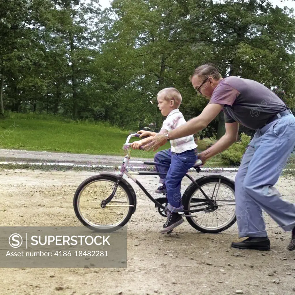 1960s MAN FATHER GIVING BOY SON ON BIKE A PUSH TEACHING HIM HOW TO RIDE BICYCLE