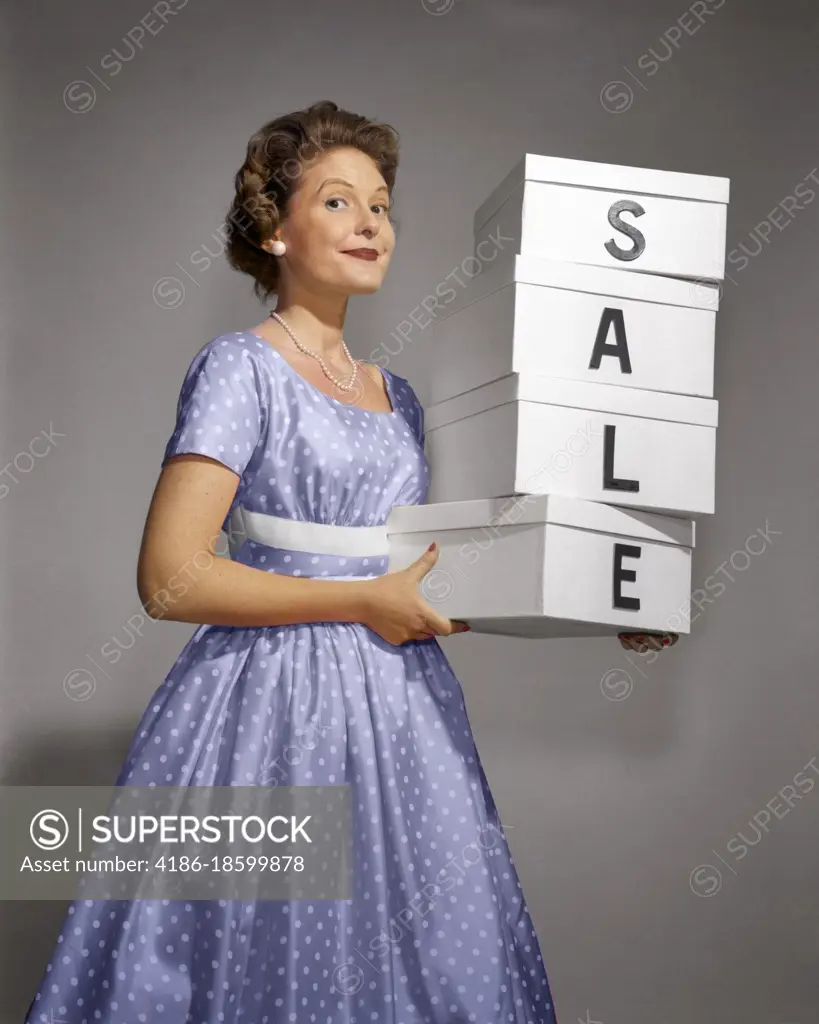 1960s WOMAN IN POLKA-DOT DRESS LOOKING AT CAMERA HOLDING A STACK OF 4 BOXES WITH ONE CHARACTER CENTERED ON EACH SPELLING SALE