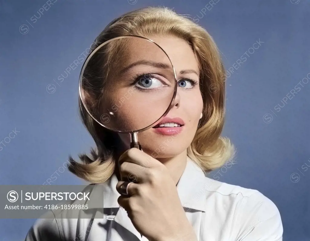 1960s BLOND WOMAN MAGNIFYING GLASS HELD UP TO AND ENLARGING ONE EYE
