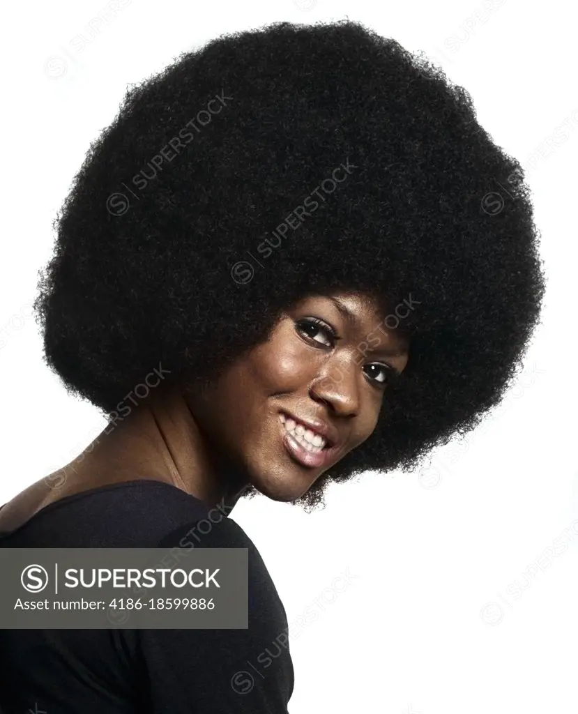 1970s PORTRAIT OF SMILING AFRICAN AMERICAN WOMAN WITH LARGE AFRO HAIR STYLE LEANING FORWARD LOOKING AT CAMERA OVER SHOULDER