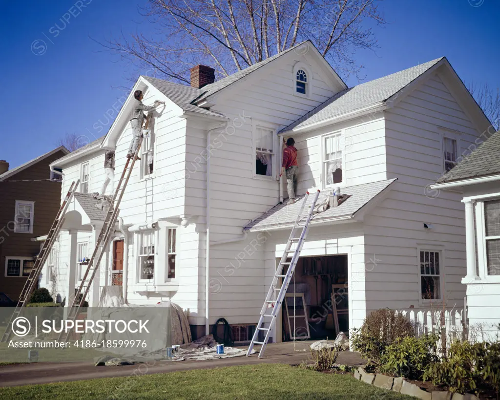 1970s FOUR MEN PROFESSIONAL CREW PAINTING THE EXTERIOR OF A WHITE WOODEN CLAPBOARD TWO STORY SUBURBAN HOUSE