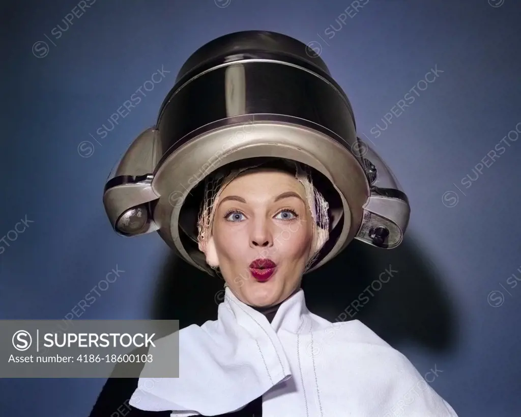 1950s SURPRISED WOMAN SITTING UNDER HAIR DRYER WITH TOWEL ON SHOULDERS AND HAIR NET LOOKING AT CAMERA