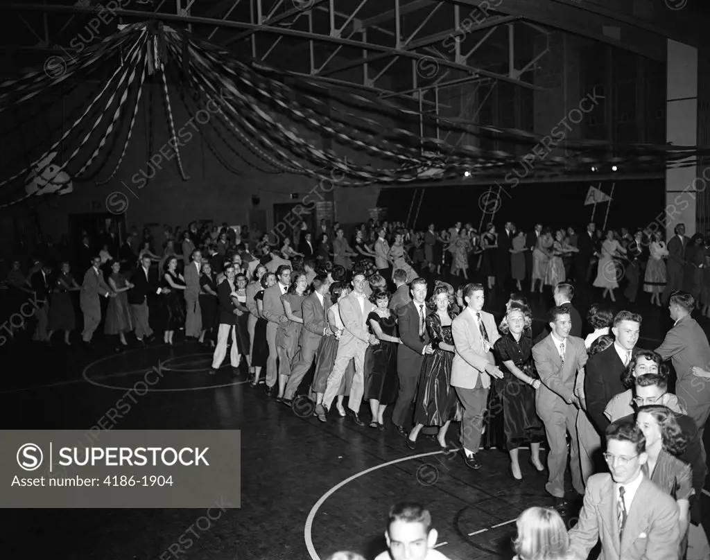 1950S High School Dance With Large Crowd Of Teen Couples In A Conga Line Snaking Through The Gymnasium