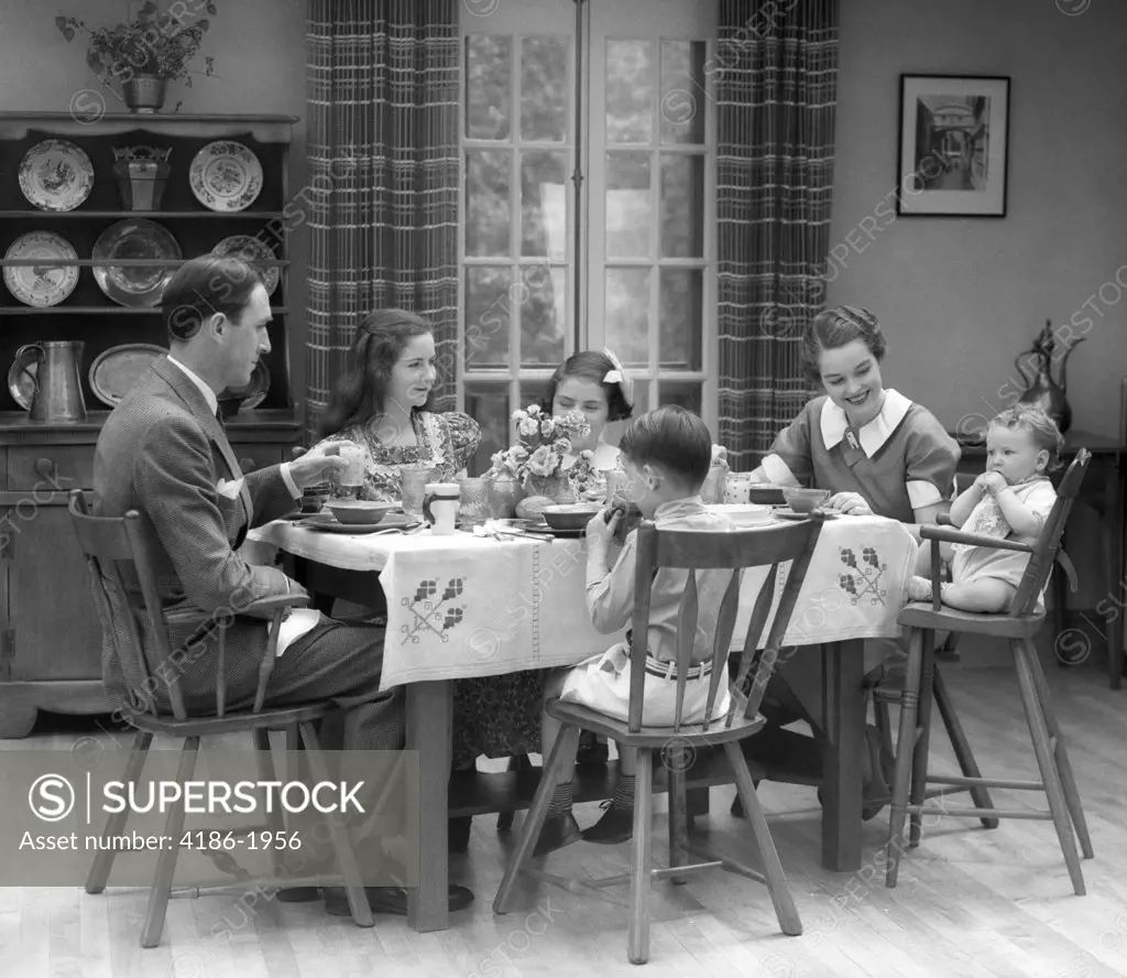 1930S Family Of 6 Sitting At The Table In A Dining Room Eating Breakfast The Baby Is Sitting In A High Chair