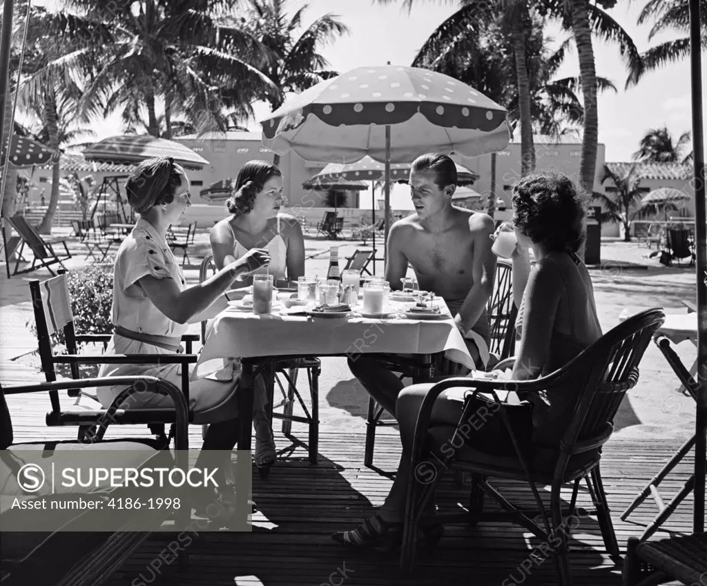 1950S Three Women And One Man Sitting At Tropical Pool Side Table Talking