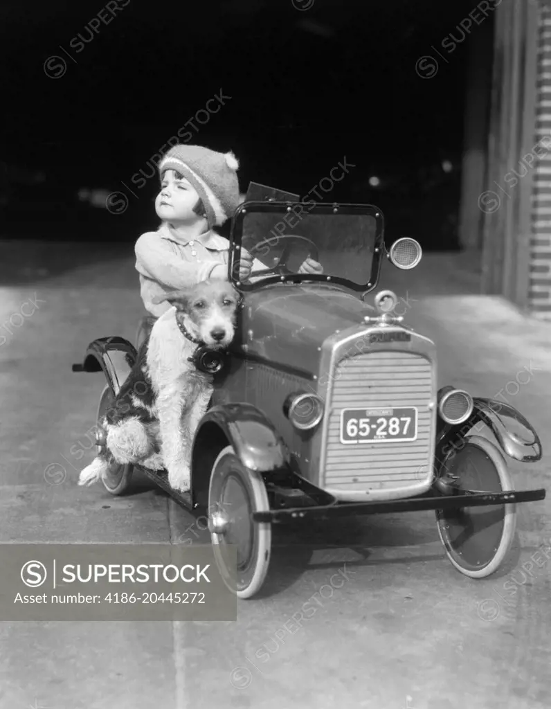 1920s GIRL IN TOY PEDAL CAR WITH DOG SITTING ON RUNNING BOARD GIRL LOOKING TO SIDE HEAD UP