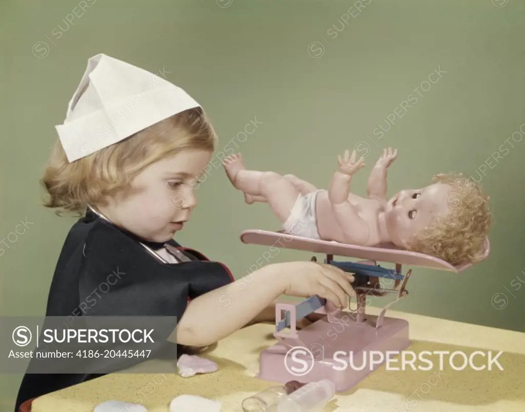 1960s LITTLE GIRL DRESSED IN NURSE'S COSTUME WEIGHING HER DOLL ON TOY BABY SCALE