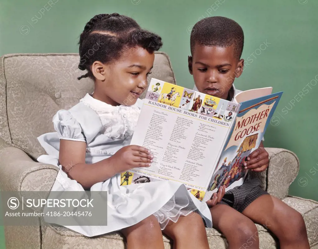 1960s AFRICAN AMERICAN BOY AND GIRL SITTING IN EASY CHAIR READING BOOK OF MOTHER GOOSE RHYMES