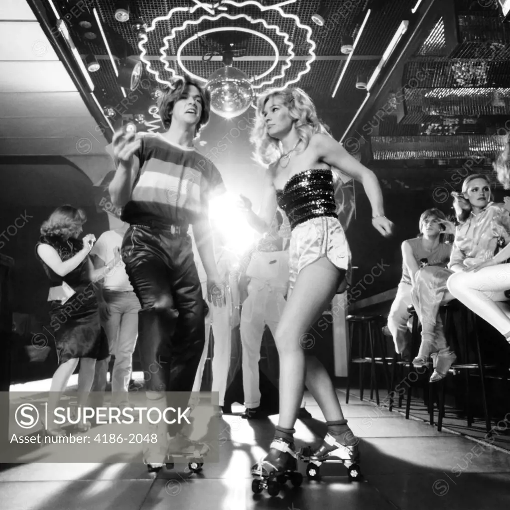 1970S Couple Disco Dancing On Roller Skates Wearing Trendy Clothes Under A Mirrored Ball