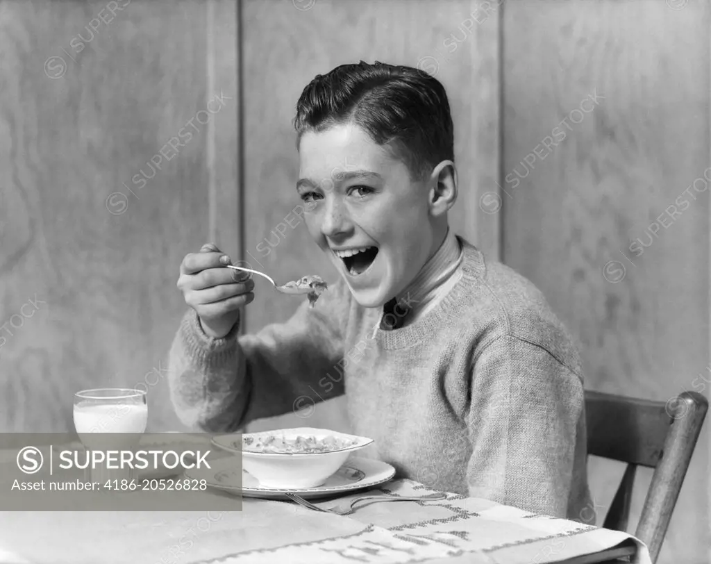 1930s 1940s SMILING BOY LOOKING AT CAMERA EATING BREAKFAST BOWL OF CEREAL AND GLASS OF MILK
