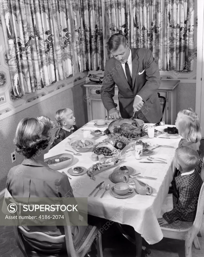 1950S Family Of 5 At Dining Room Table For Thanksgiving Dinner With Father Carving Turkey