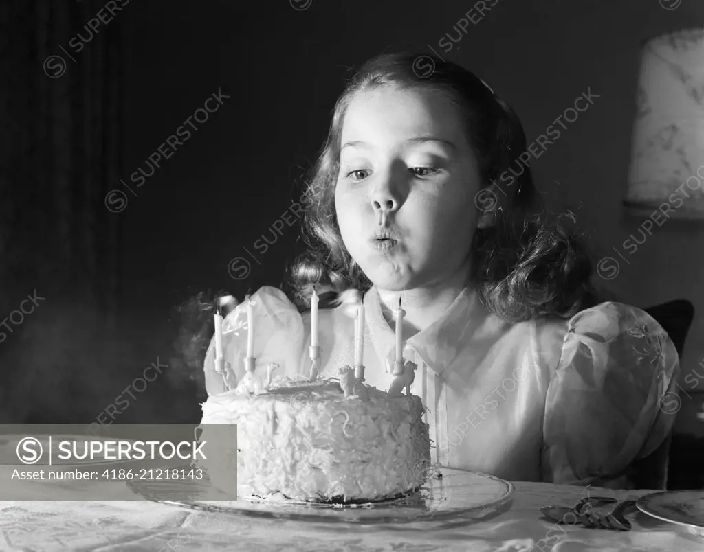 1950s GIRL IN PARTY DRESS BLOWING OUT CANDLES ON BIRTHDAY CAKE WITH 5 CANDLES
