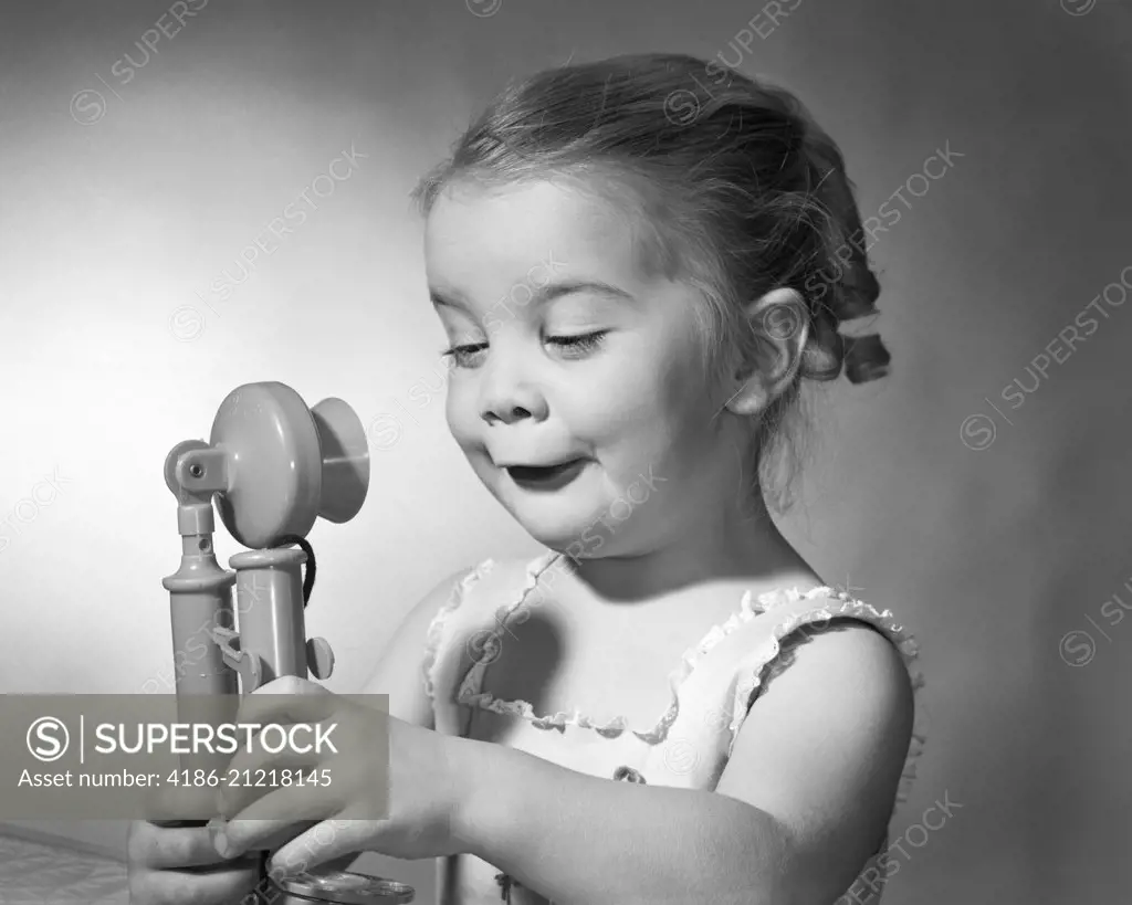 1960s LITTLE GIRL WITH FUNNY FACIAL EXPRESSION HOLDING A TOY CANDLE STICK TELEPHONE IN BOTH HANDS