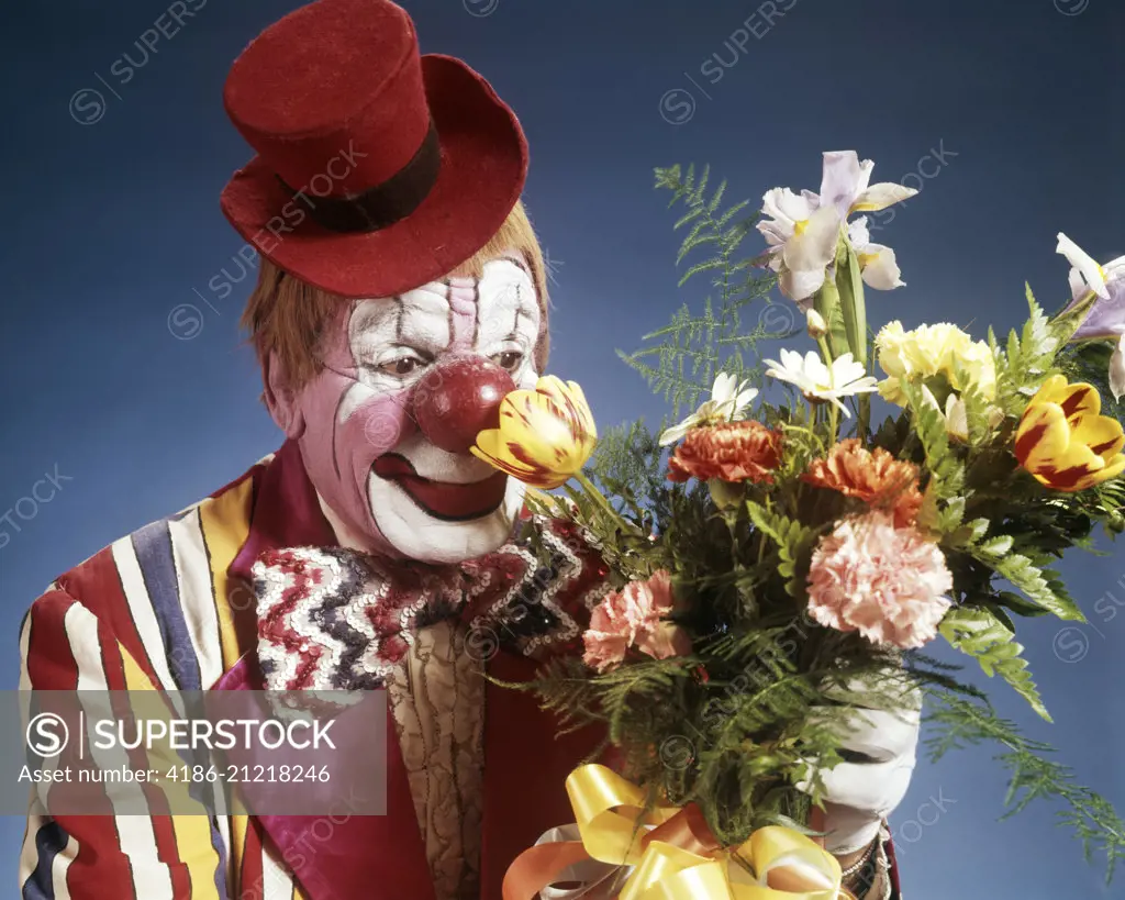 1970s PORTRAIT HAPPY CIRCUS CLOWN WEARING TINY RED TOP HAT STRIPED COSTUME BIG BOW TIE SMELLING BOUQUET OF FLOWERS