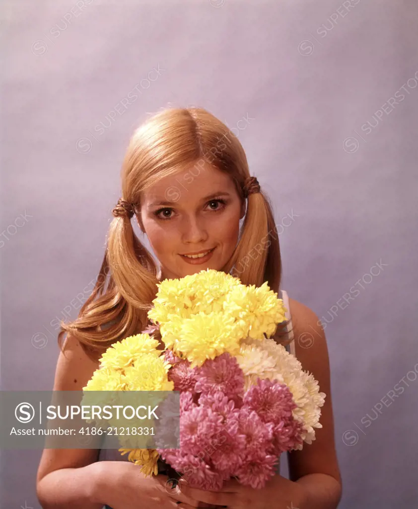 1970s YOUNG WOMAN GIRL ATTRACTIVE BLOND BLONDE HOLDING BOUQUET FLOWERS YELLOW PINK PIGTAILS LOOKING AT CAMERA