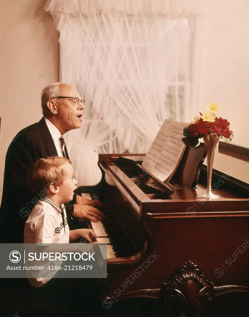 1970s ELDERLY GRANDFATHER AND YOUNG GRANDSON SINGING AND PLAYING A GRAND PIANO TOGETHER