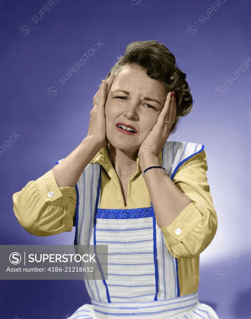 1950s WOMAN IN COTTON DRESS WITH BOTH HANDS OVER HER EARS HOLDING HER HEAD FROWNING LOOKING AT CAMERA