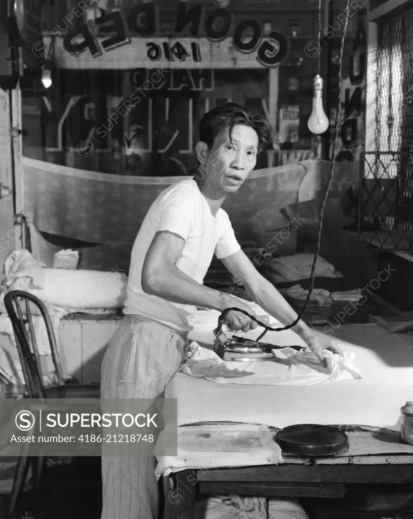1920s CHINESE LAUNDRY MAN LOOKING AT CAMERA IRONING CLOTHES ON BOARD