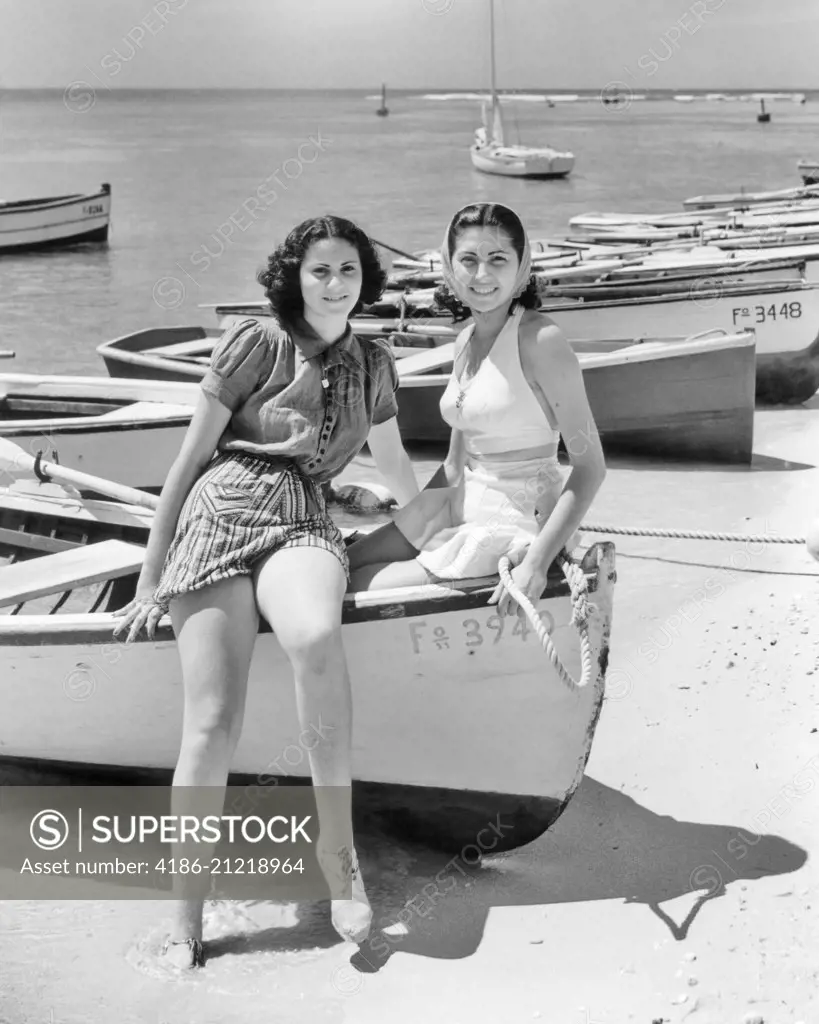 1930s 1940s TWO SMILING WOMEN SITTING ON BOW OF ROWBOAT WEARING BEACH CLOTHES LOOKING AT CAMERA LA PLAYA HAVANA CUBA