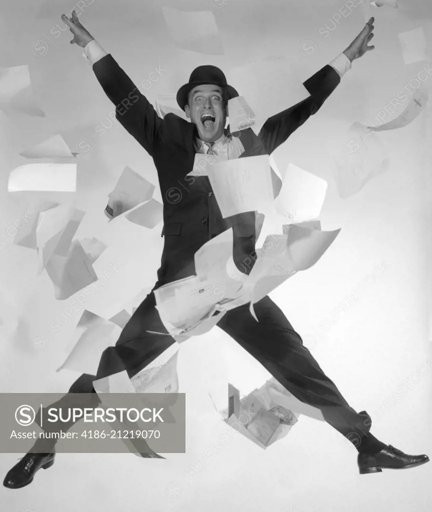 1950s 1960s HAPPY MAN SALESMAN BUSINESSMAN SUIT TIE HAT JUMPING IN AIR PAPERS FLYING ALL AROUND LOOKING AT CAMERA