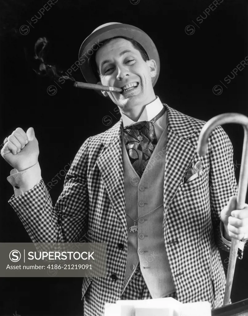 1930s SMILING MAN CARNIVAL BARKER CON MAN IN CHECKERED SUIT WITH CANE IN HAND & CIGAR IN MOUTH LOOKING AT CAMERA