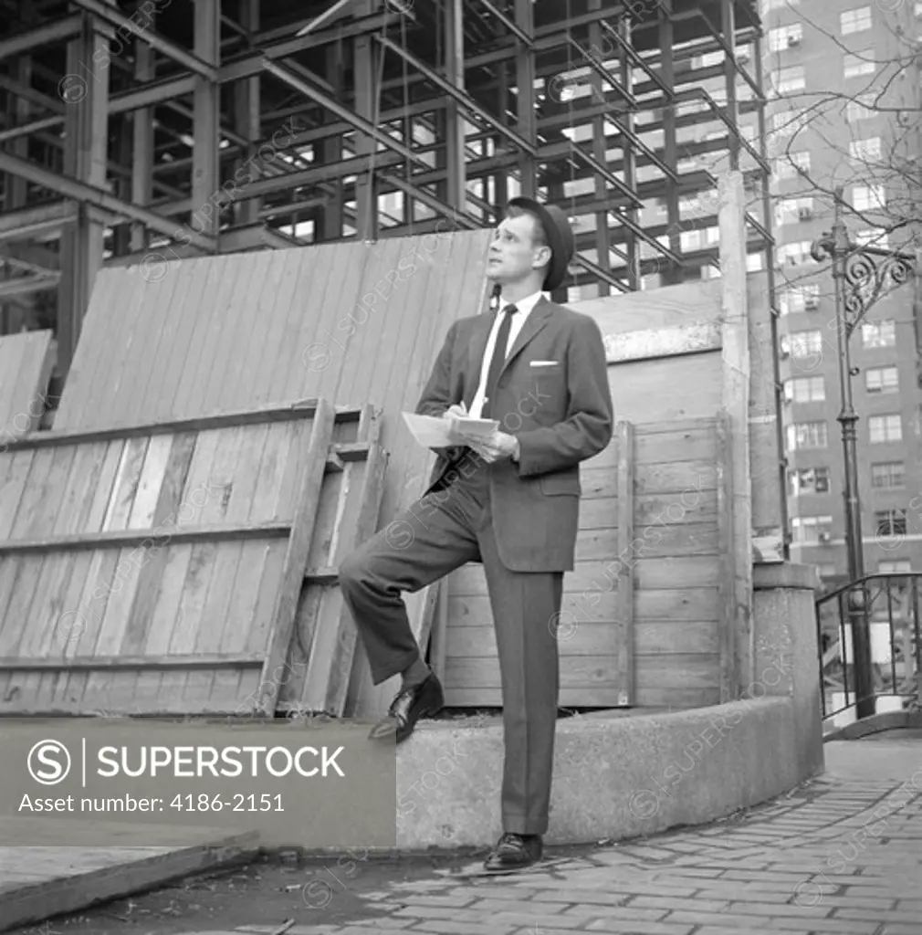 1960S Businessman On Curb Looking Up Into Building Under Construction Writing Notes
