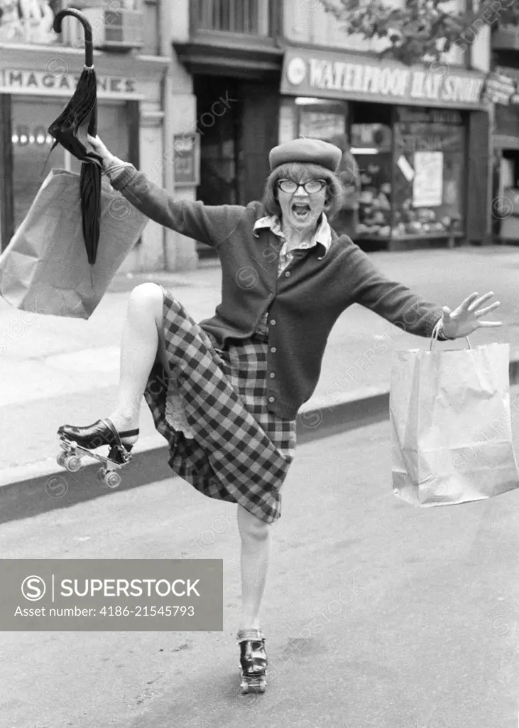 1970s CRAZY WILDLY GESTURING SHOPPING BAG LADY WOMAN ON ROLLER SKATES ON CITY STREET LOOKING AT CAMERA 