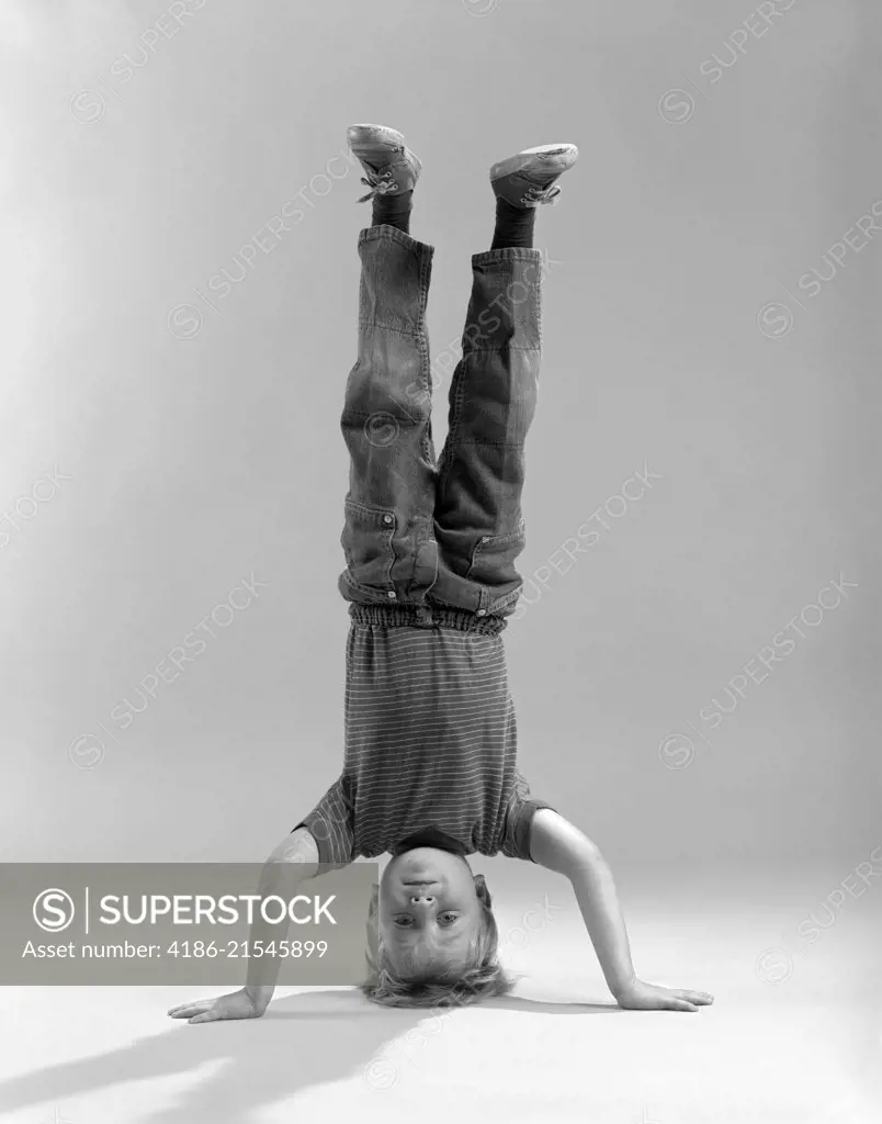 1960s BOY STANDING ON HIS HEAD LOOKING AT CAMERA