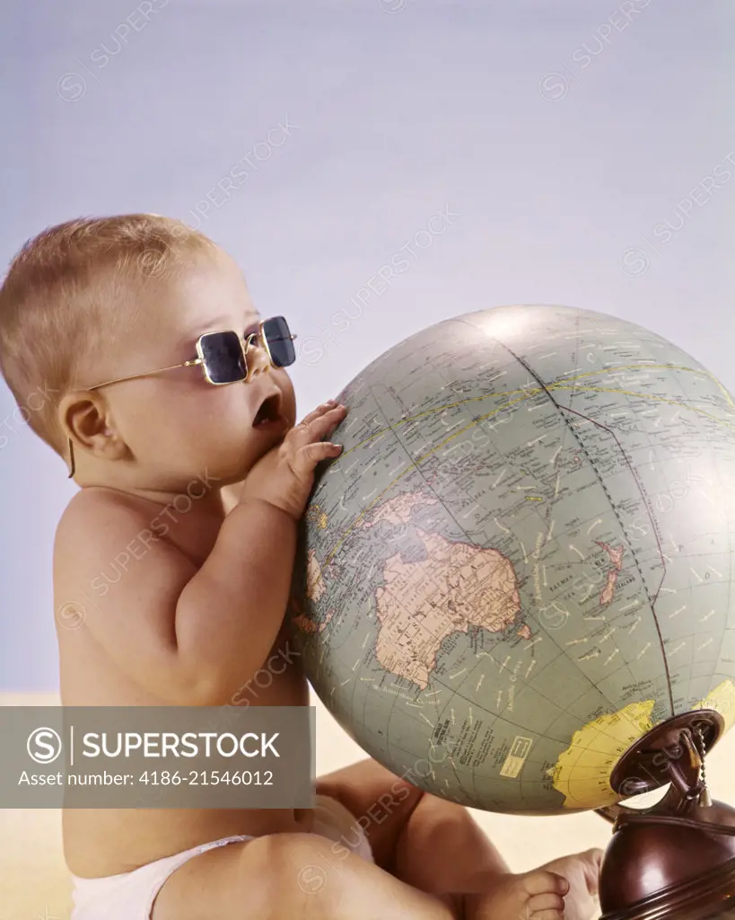 1960s BABY WEARING SUNGLASSES LOOKING LOOKING AT WORLD GLOBE MAP