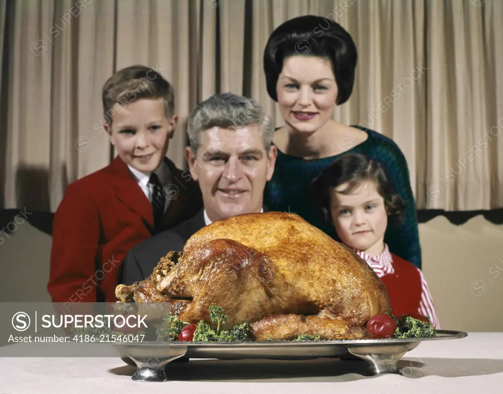 1960s PORTRAIT OF FAMILY FATHER MOTHER SON DAR LOOKING AT THANKSGIVING OR CHRISTMAS ROAST TURKEY