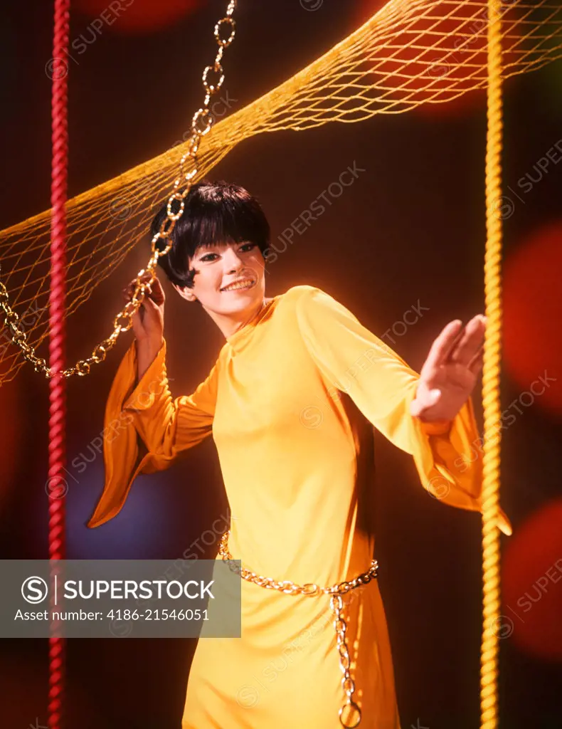 1960s YOUNG WOMAN WEARING YELLOW DRESS CHAIN BELT DISCO DANCING LOOKING AT CAMERA