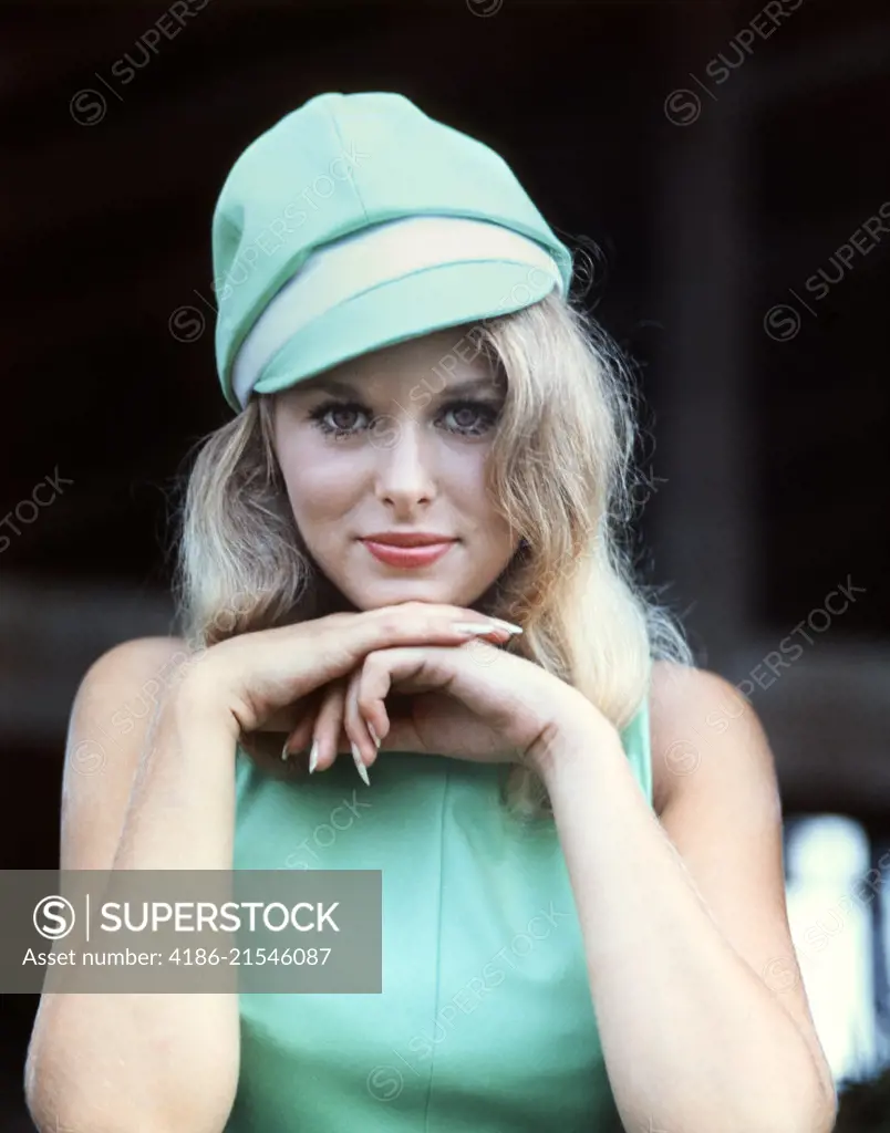 1960s SEXY BLONDE WOMAN PORTRAIT CHIN RESTING ON HANDS TURQUOISE BLUE DRESS & SILLY MOD FASHION CAP HAT