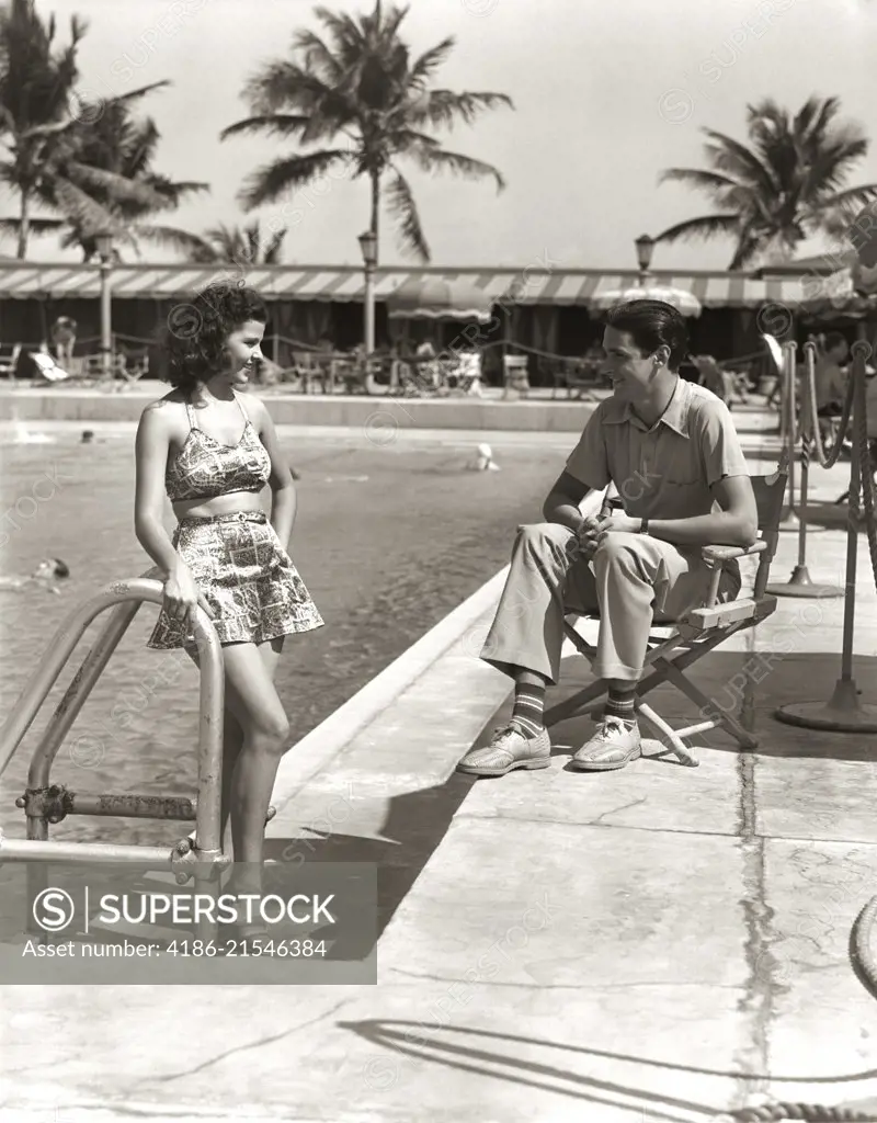 1930s COUPLE TROPICAL HOTEL SWIMMING POOL SIDE WOMAN BATHING SUIT MAN SITTING DIRECTORS CHAIR CASUAL CLOTHES MIAMI BEACH FL USA