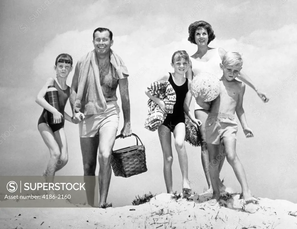 1960S Family Walking Over Sand Dune At Beach Carrying Picnic Basket