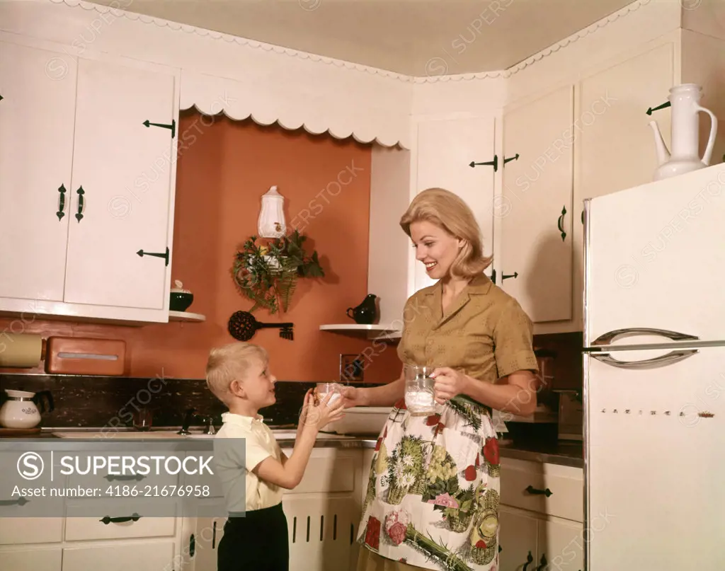 1970s BLONDE MOTHER GIVING SON GLASS MILK IN KITCHEN  